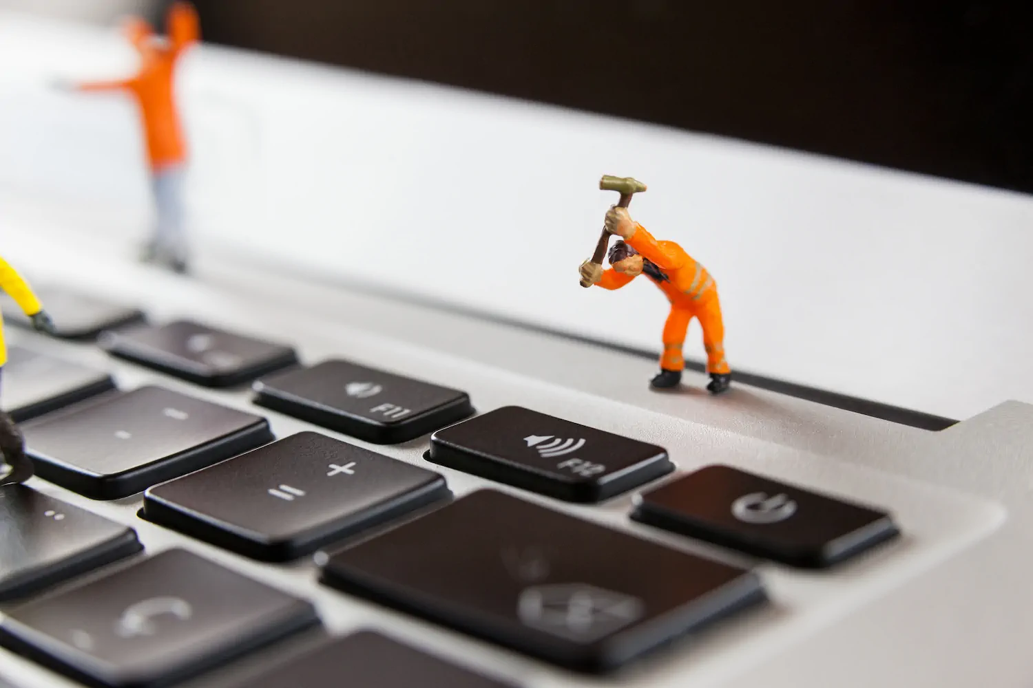 Figura miniatura de trabajador con martillo sobre teclado, concepto de reparación y refuerzo de seguridad en páginas web.