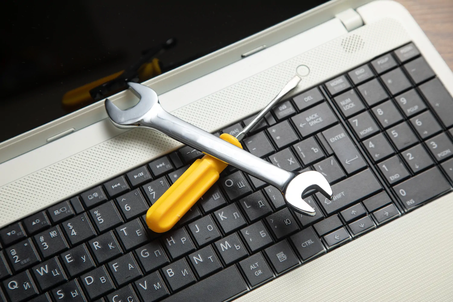 Llave inglesa y desarmador sobre teclado de laptop, representando mantenimiento técnico y seguridad informática.