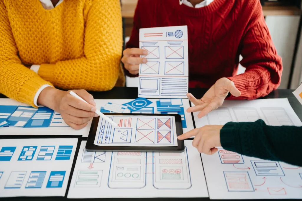 Diseñadores revisando wireframes y prototipos en papel y tablet para crear un diseño web responsivo y profesional.