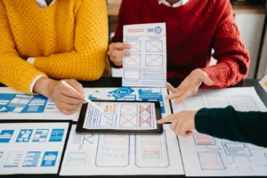 Diseñadores revisando wireframes y prototipos en papel y tablet para crear un diseño web responsivo y profesional.
