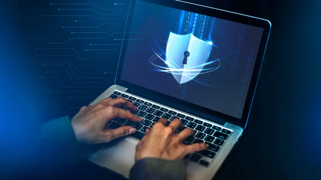 Manos tecleando junto a icono de ciberseguridad en portátil