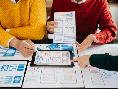 Diseñadores revisando wireframes y prototipos en papel y tablet para crear un diseño web responsivo y profesional.